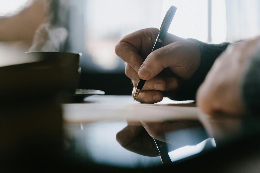 A hand writes on a sheet of paper with a pen.