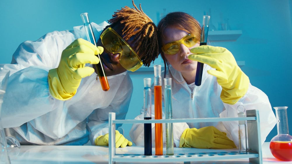 Two scientists look at bright-colored liquids in long test tubes.