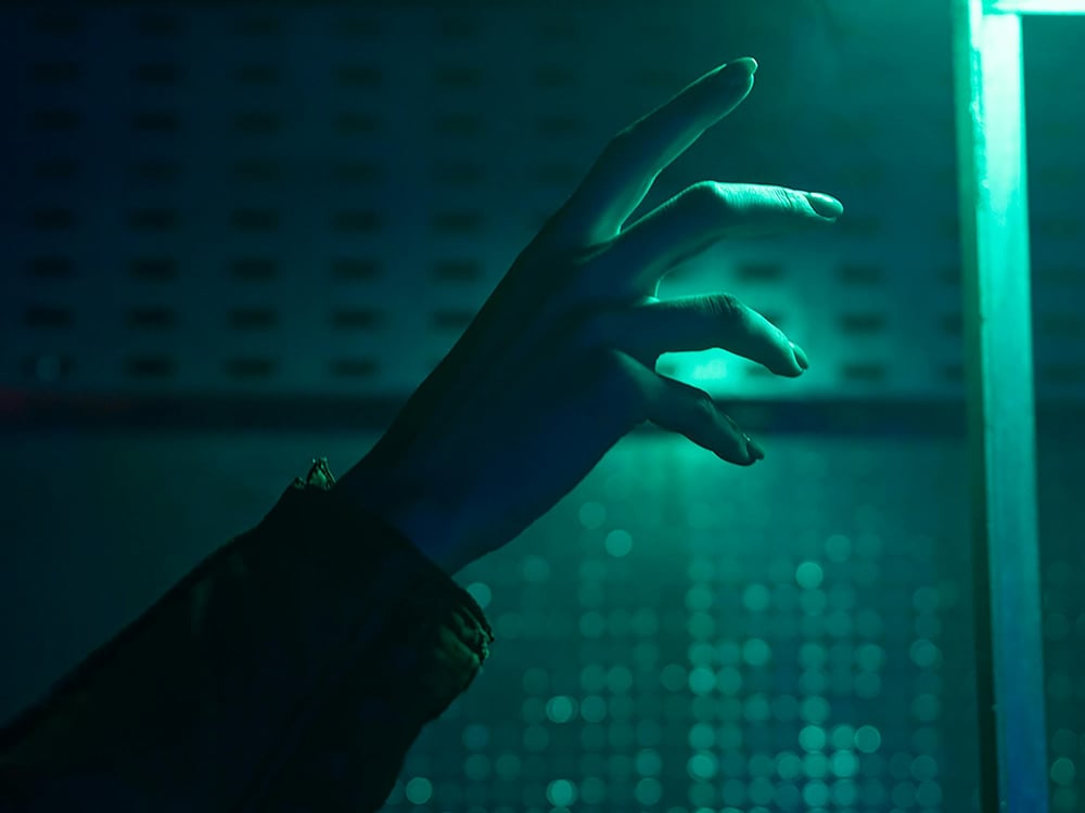 A hand reaches out in the darkness, lit by an eerie green light.