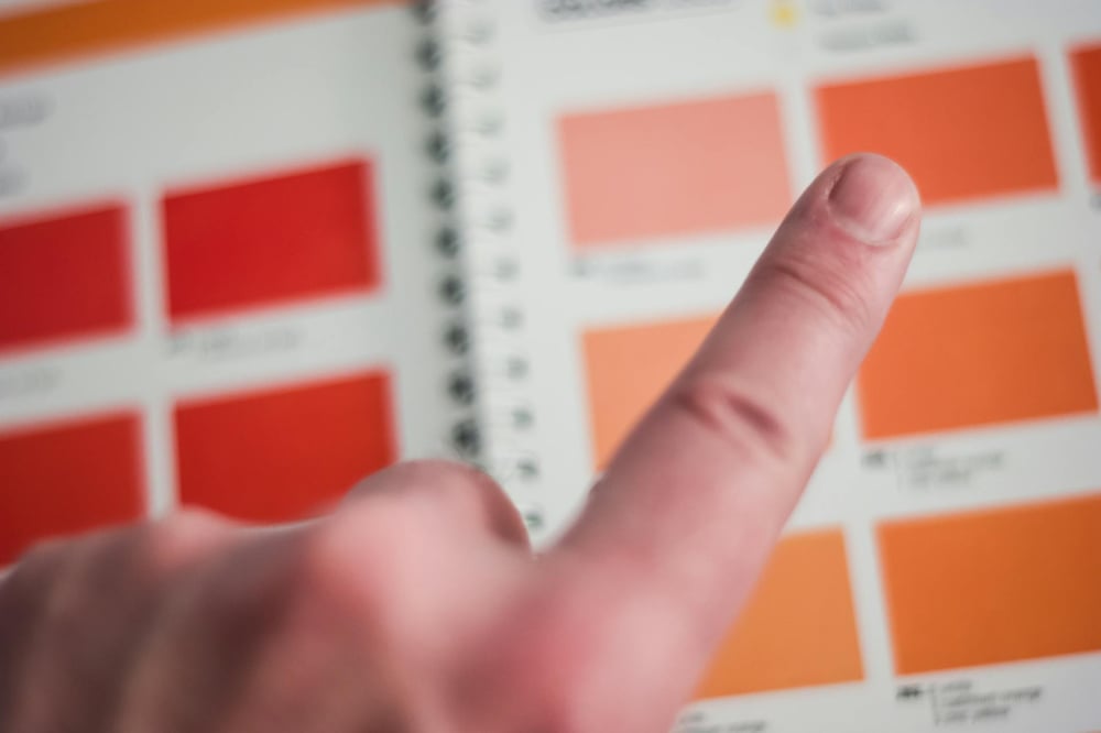 A finger hovers over a page of paint chips in different shades of orange and red.