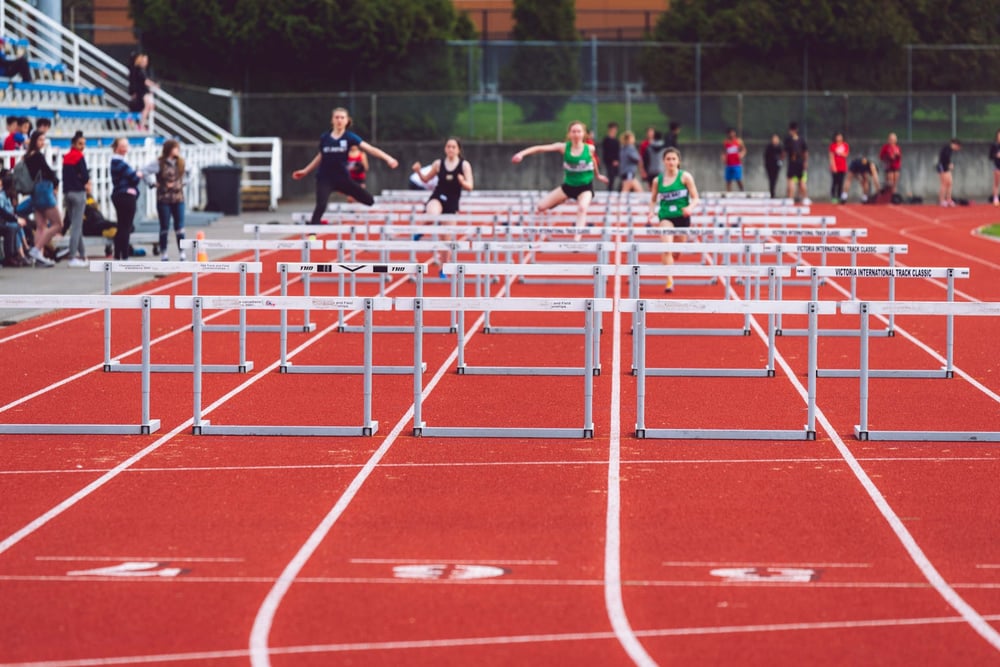 Runners jump over a long row of hurdles.