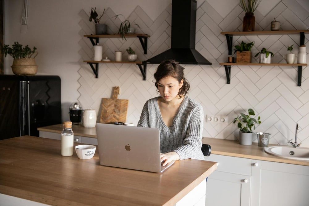 A person sits at a kitchen island, staring at a laptop screen.