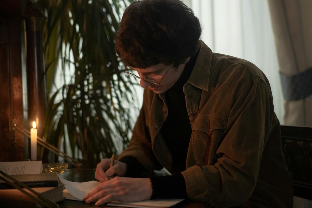 A person writes by candlelight in a dark room.