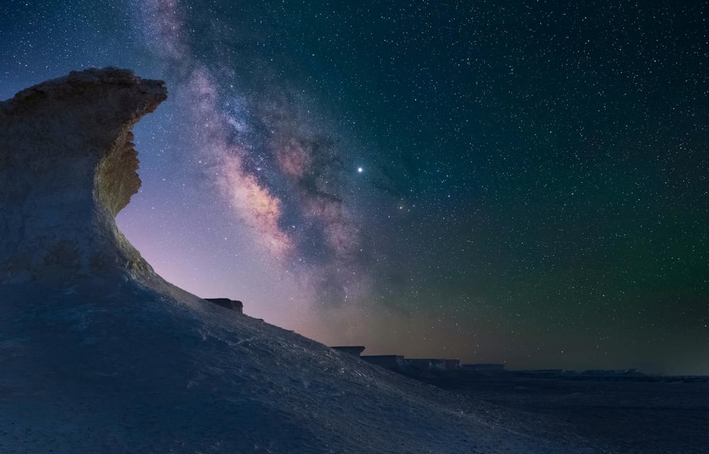 A dark fantasy style landscape—dark and deserted with the milky way above an unusual, wave-shaped rock formation.