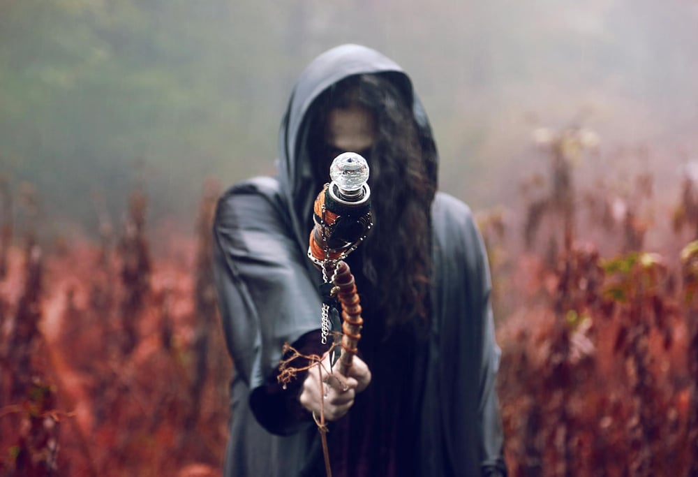 A warlock in a dark clock reaches out with a crooked scepter.