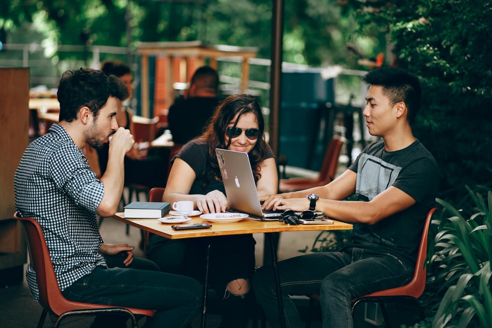 Three writers hang out together at a small outdoor café table.