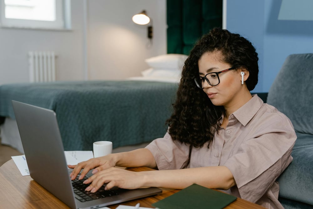 A person wearing glasses and bluetooth ear buds types on a computer.