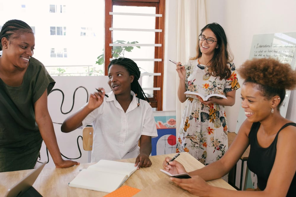 A happy group of writers all holding notebooks gather around a table.
