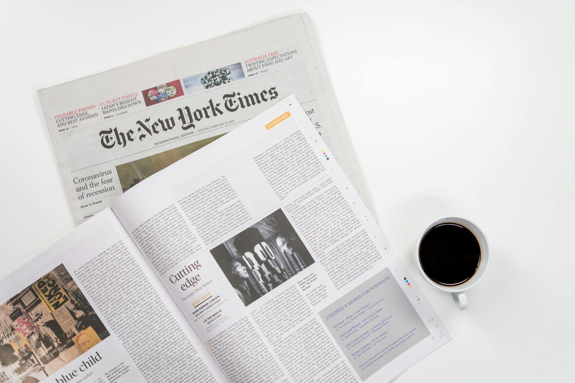 A cup of coffee sits beside an open magazine and copy of the New York Times.