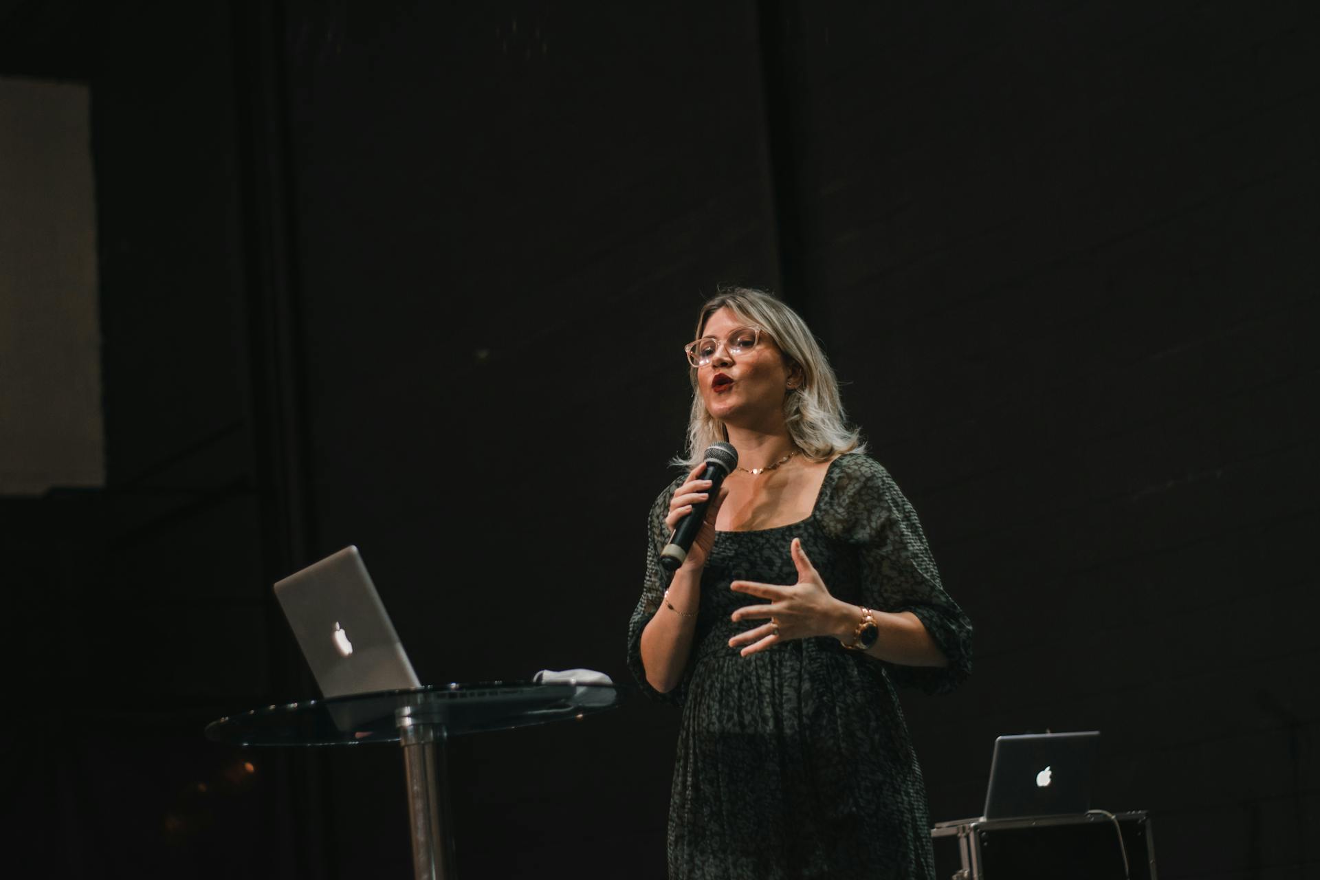 A person in a black dress stands on a stage making a speech into a microphone.