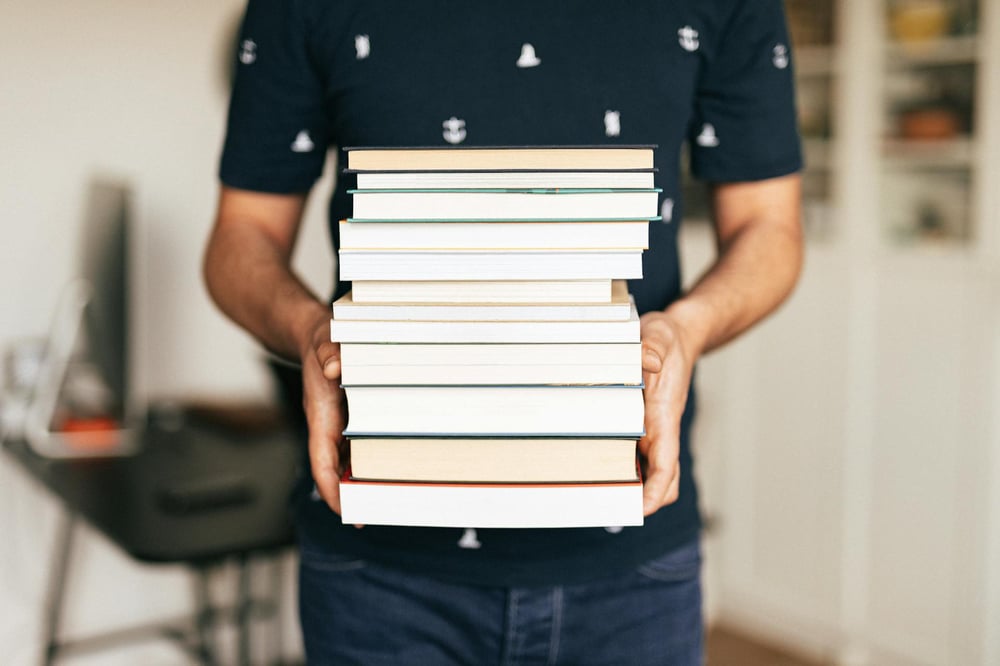 A person holds a stack of books with their spines facing away.