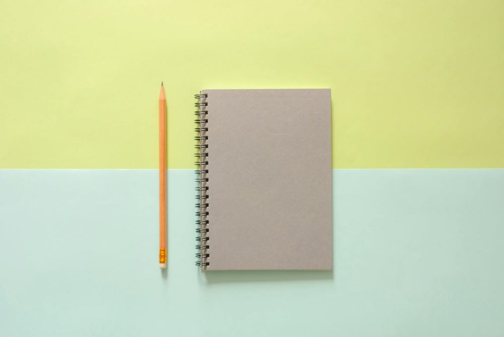 A gray notebook and yellow pencil sit on a blue and green background.