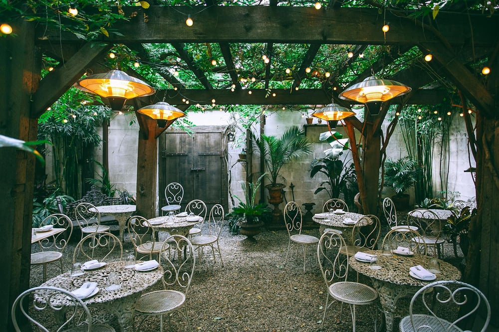 A pretty café patio with tropical plants, string lights, and white bistro tables.