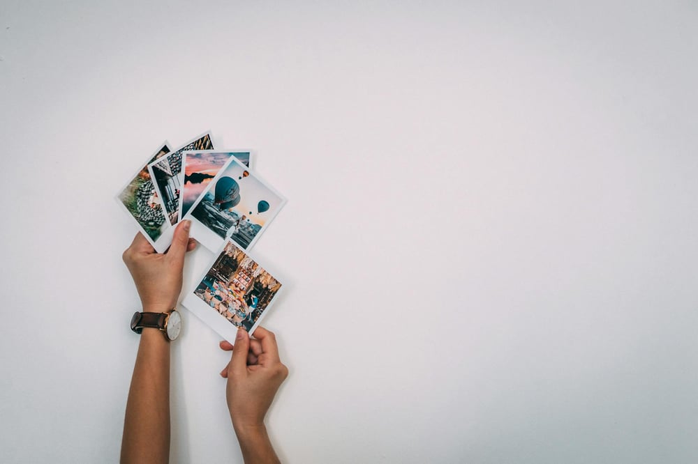 Hands hold several Polaroid photos fanned out, showing different images.
