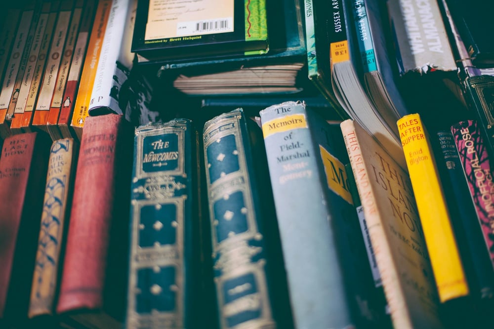 Several vintage books sit on a table side by side with their spines up.