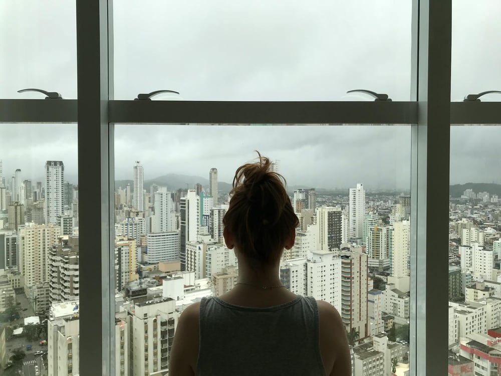 The back of a person looking out a window at a city on a cloudy day.