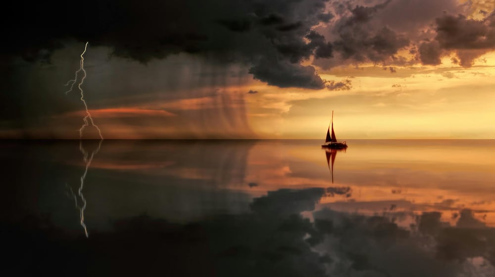 A boat drifts on glassy water at sunset as lightning strikes in the distance.
