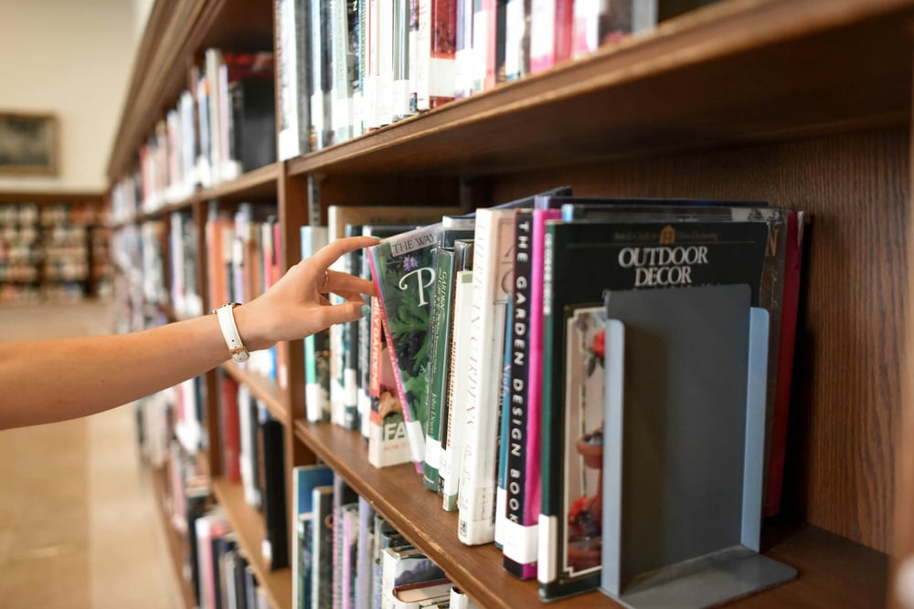 A hand pulls a book off a library bookshelf.