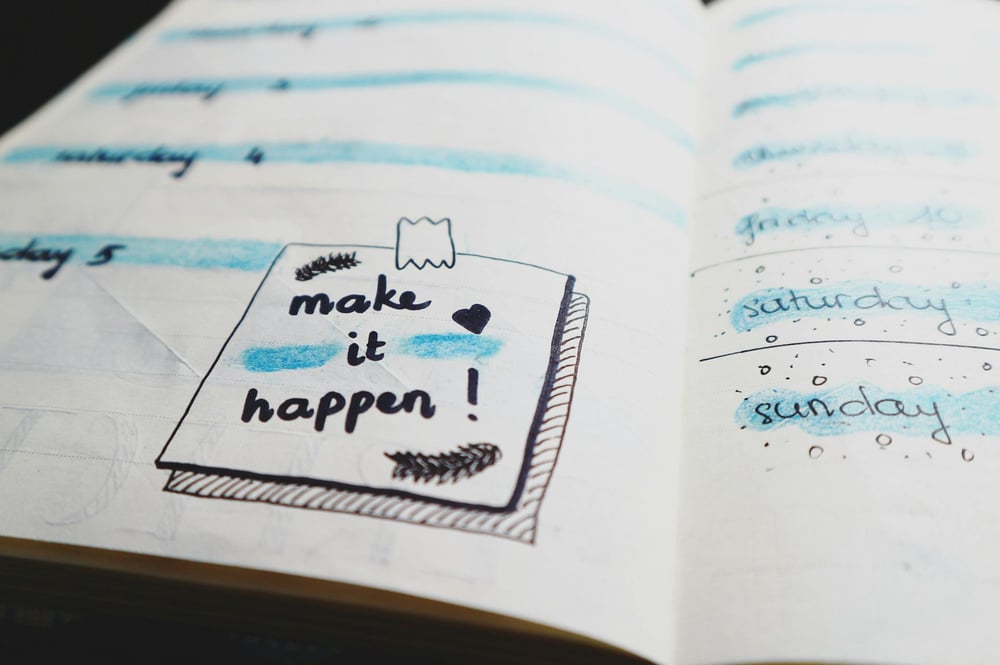 An open page in a planner with a drawn-on sticky note that says