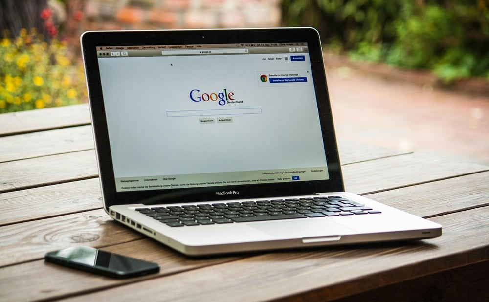 A laptop open to Google sits on an outdoor table.