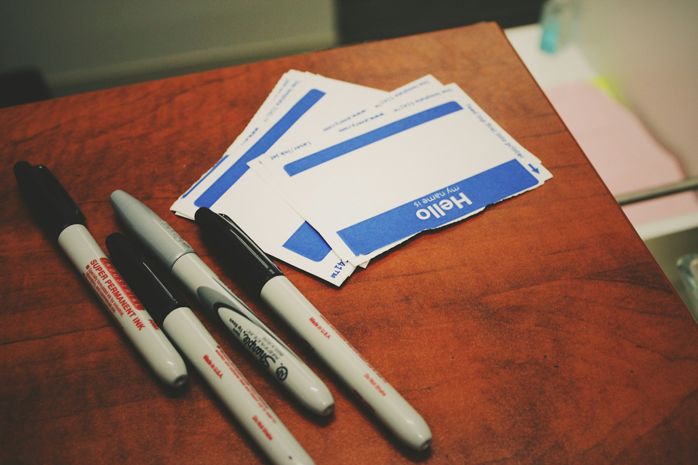 A stack of name tags sits on a table beside black and silver Sharpies.