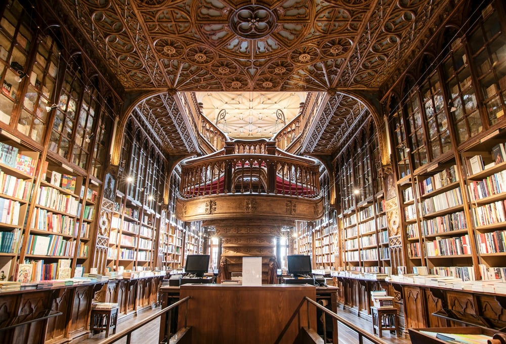 A beautiful library with two-story bookshelves and ornate detailing in the wooden ceiling.