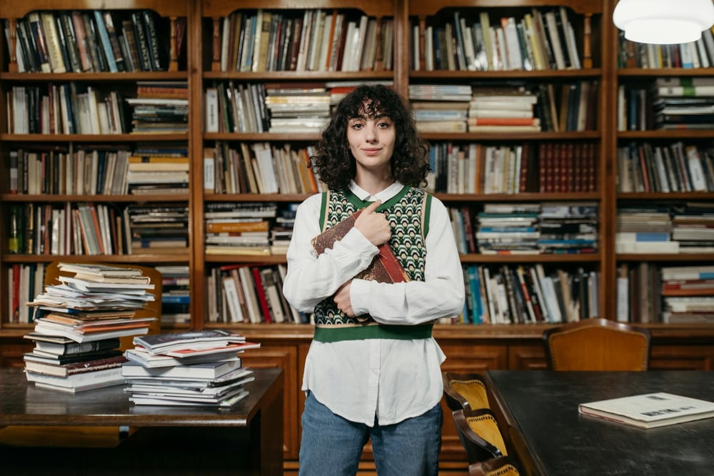 A person standing in front of desks and bookshelves piled with books clutches a book to their chest.