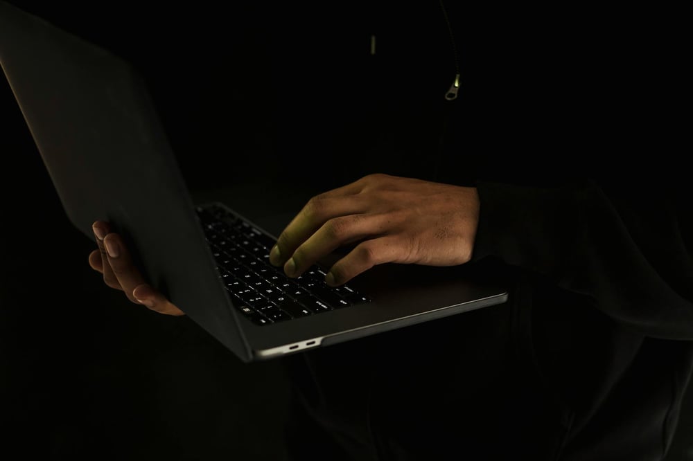 Hands typing on a dark laptop in a dark room.