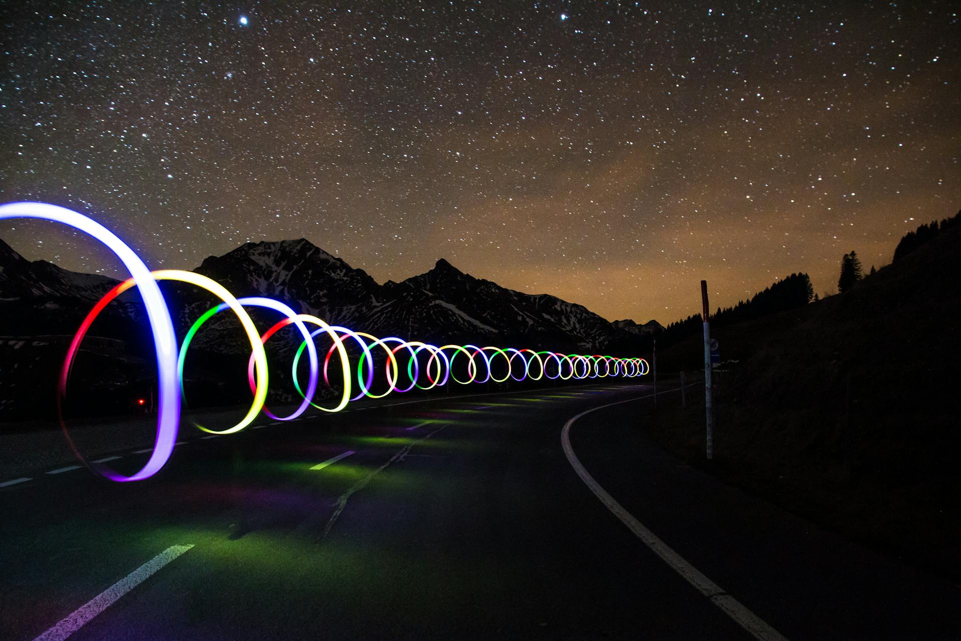 A colorful light spirals down a dark highway between mountains.