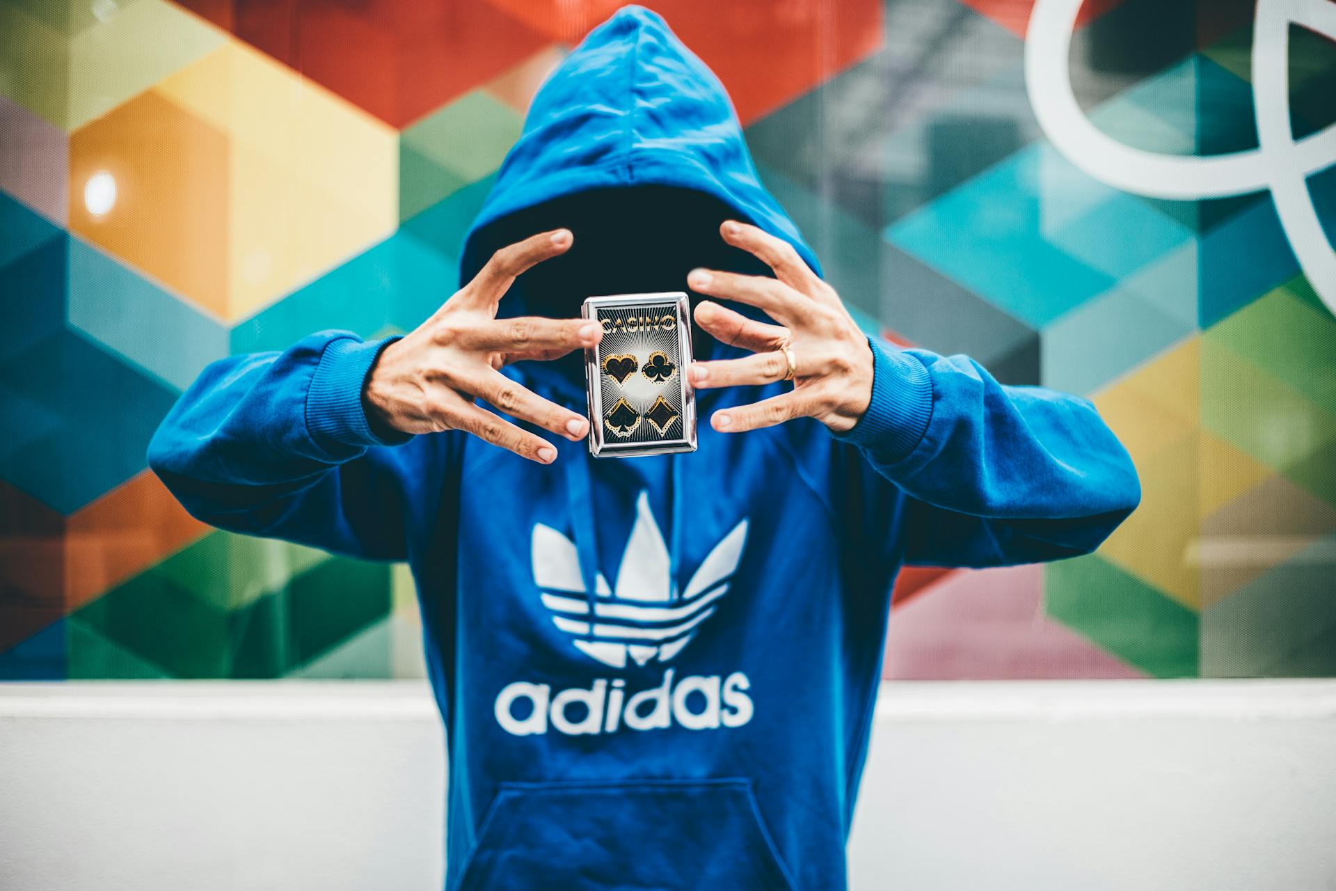 A person with the hood of a hoodie pulled down over their face makes a pack of playing cards levitate in front of them.n