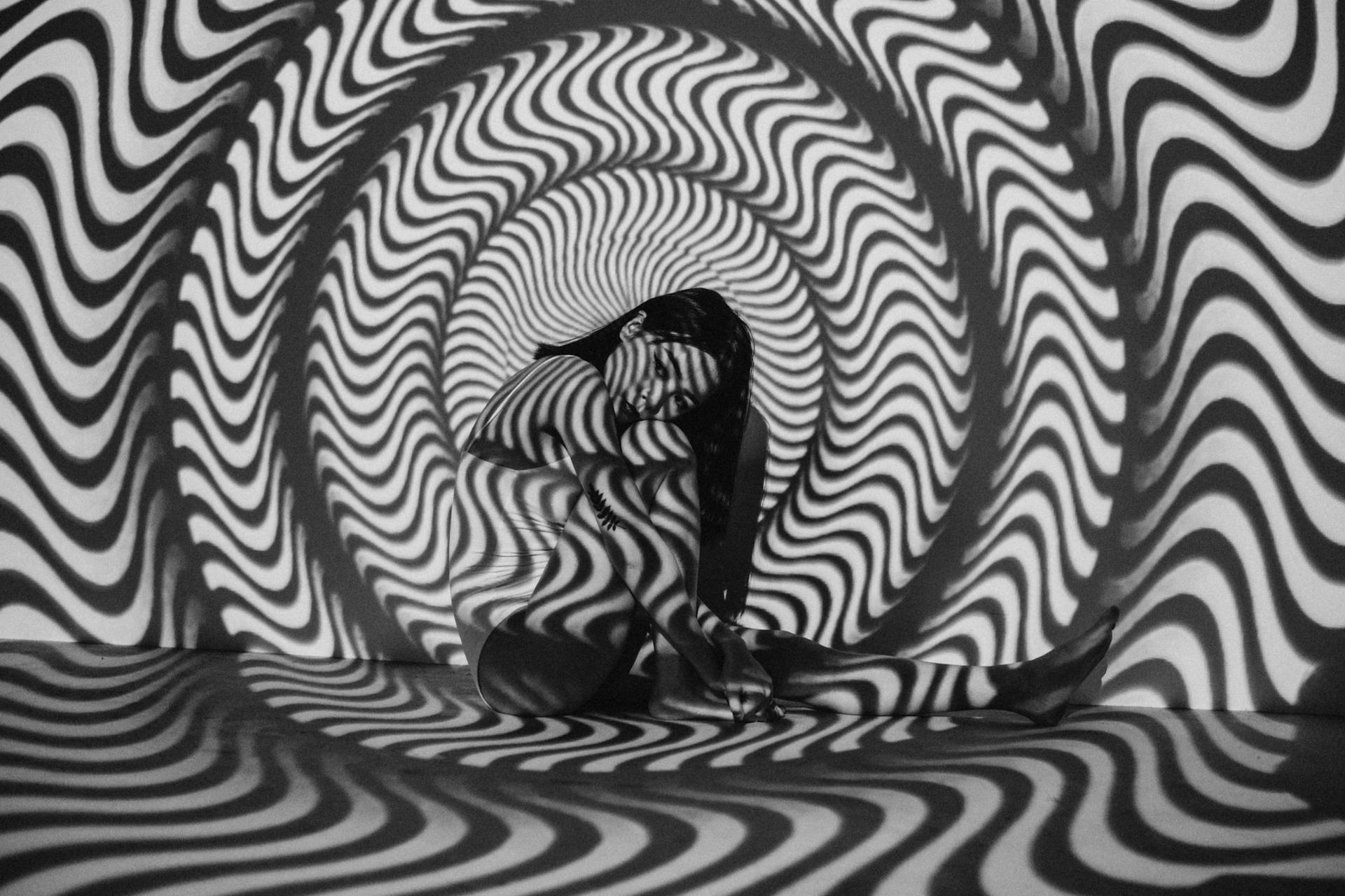 A person sits balled up on the floor with rings of squiggly black and white light projected onto them.