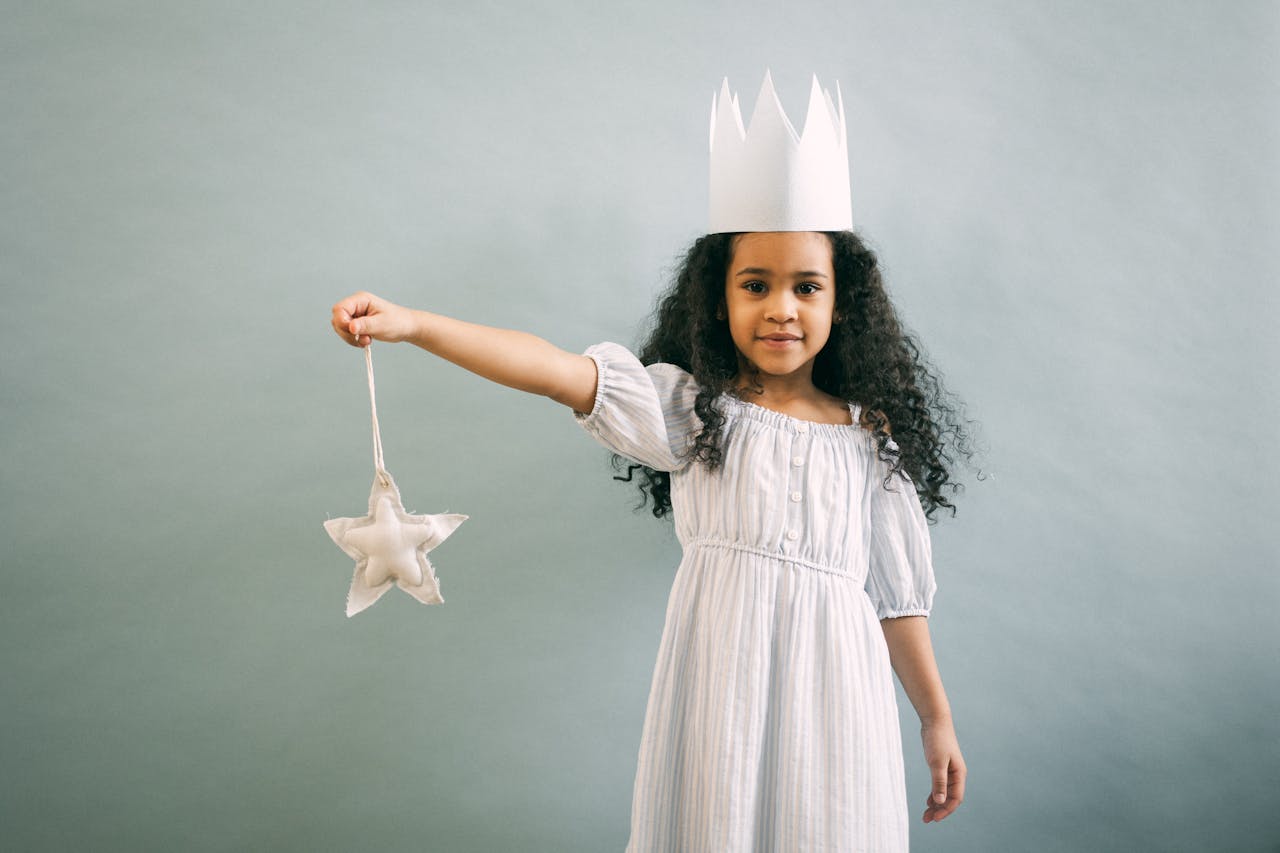 A child in crown holds out a star on a string.