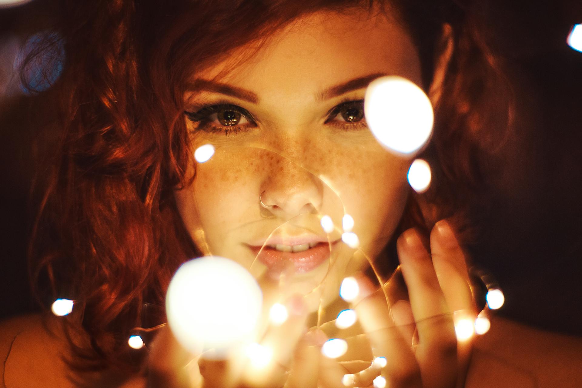 A person gazes through a cluster of fairy lights.