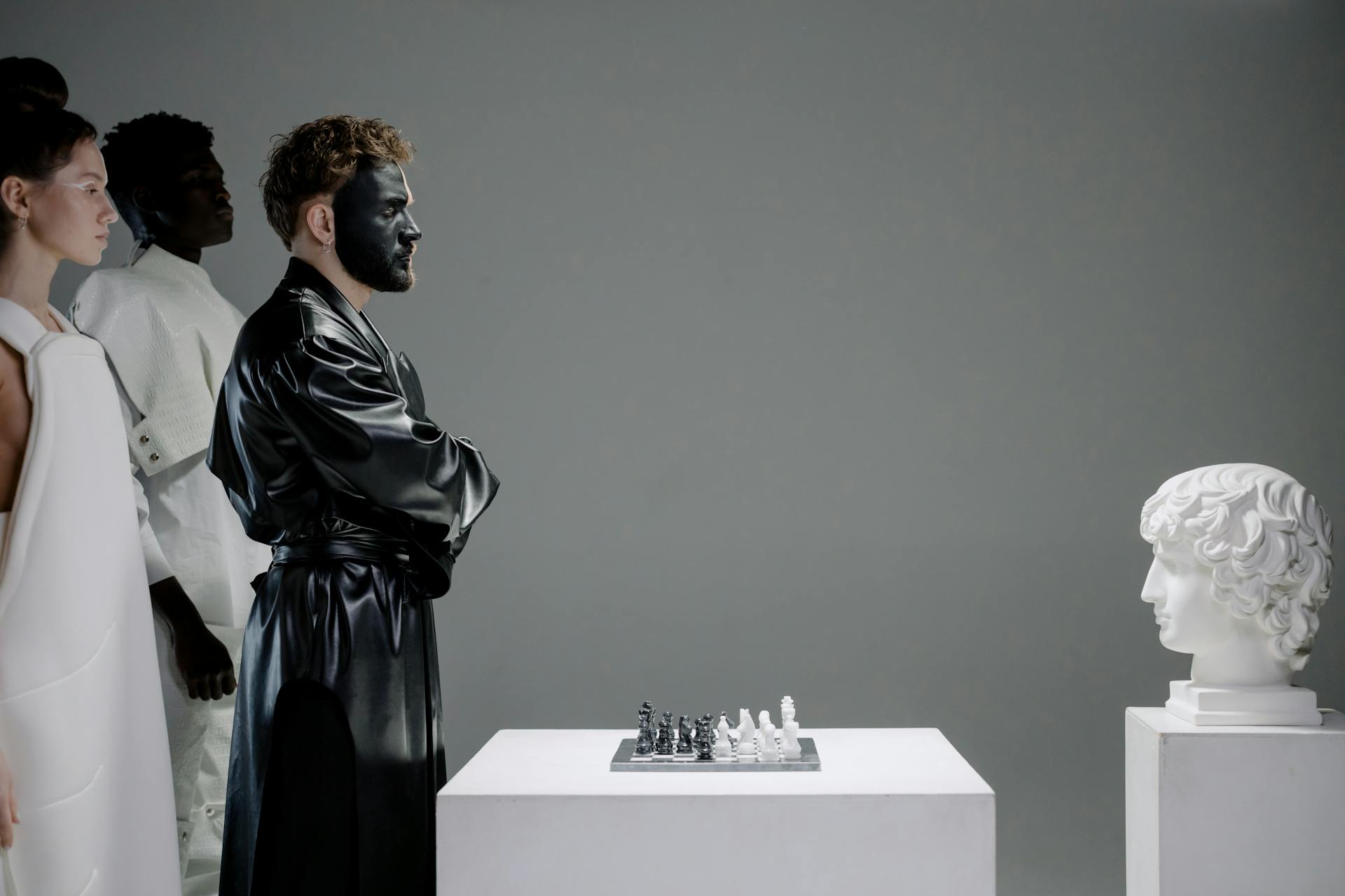 A person in a mask playing chess with a sculpture of a human head.