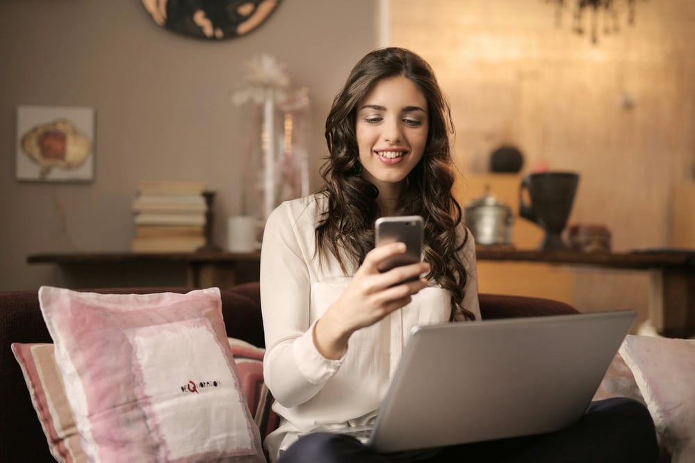A person sits in front of their computer and looks at their phone.