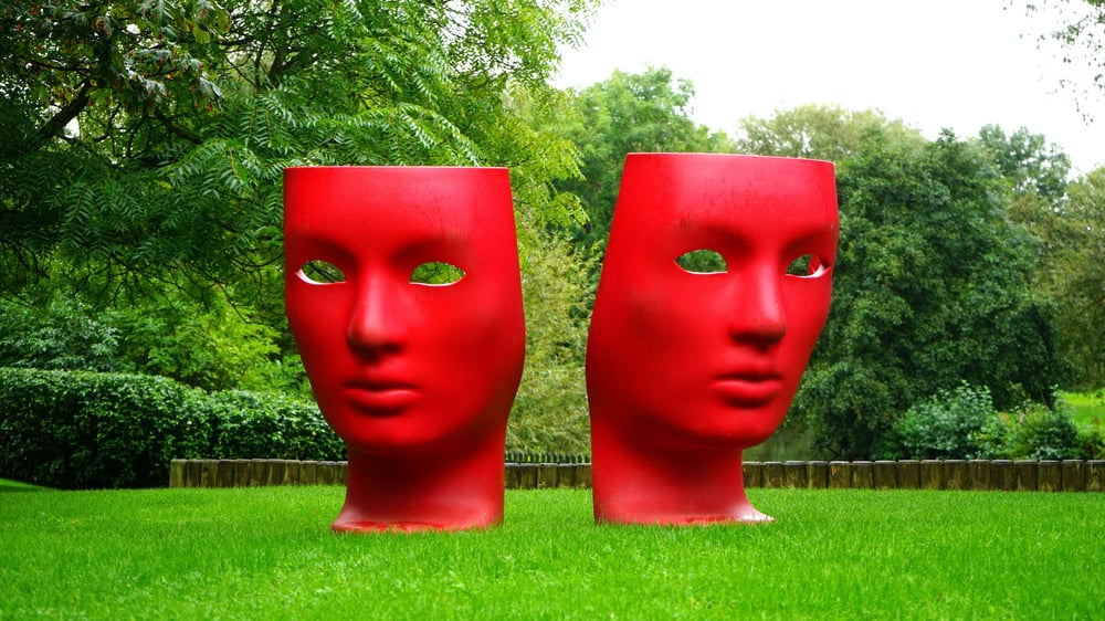 Two giant face sculptures facing opposite directions in a sculpture park.