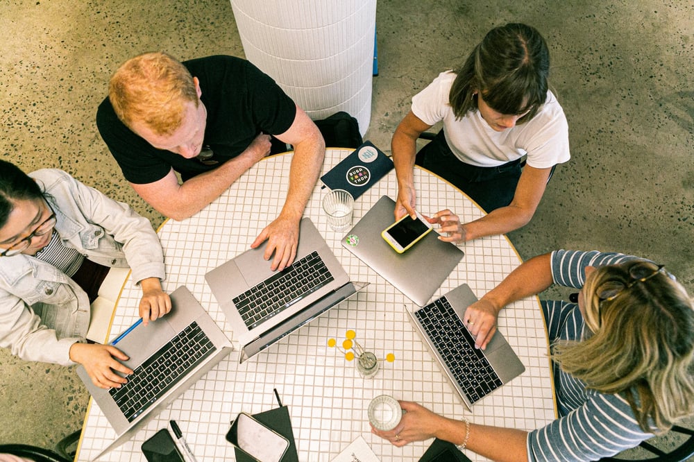 Overhead view of writers gathered around a table with laptop computers.