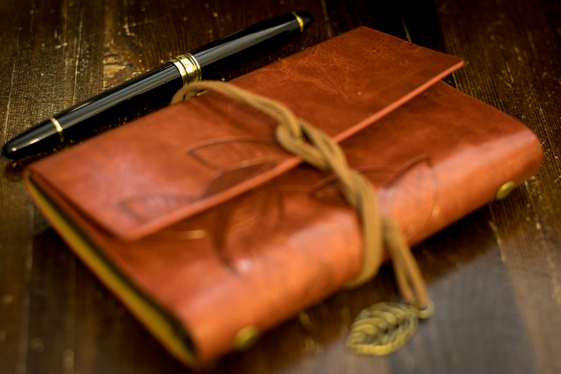 A black fountain pen sits on a dark wood desk beside a leather journal.