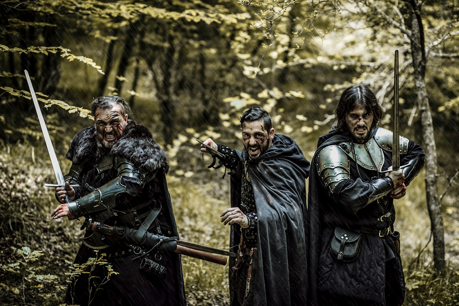 Warriors clad all in black stand in the forest holding swords and poised for battle.
