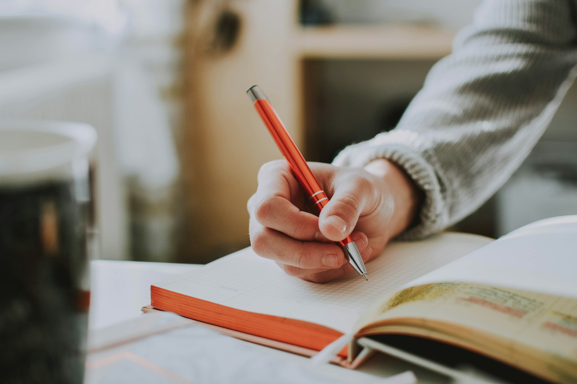 A hand writes in a notebook with a bright orange pen.