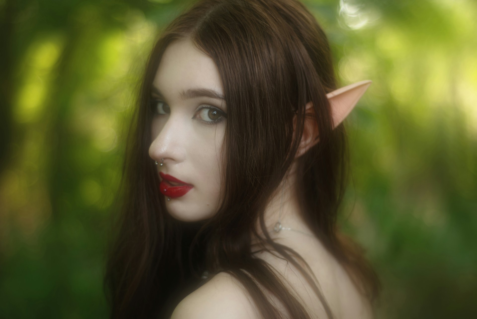 An elf or fairy with long dark hair and a nose ring looks over their shoulder.