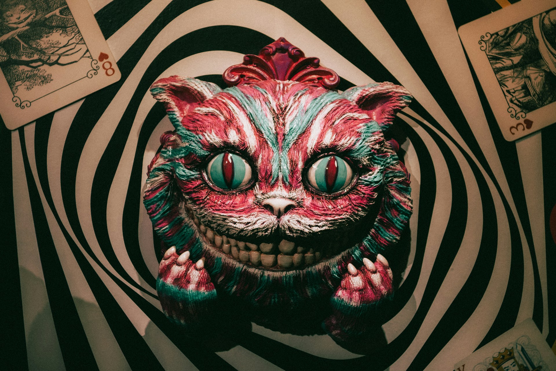 A sculpture of the Chesire Cat's head fixed onto a wall painted like a rabbit hole.