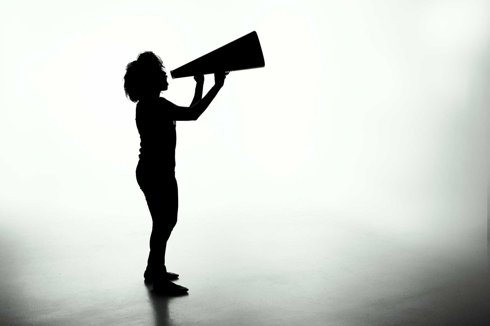 Silhouette of a person yelling into a megaphone.