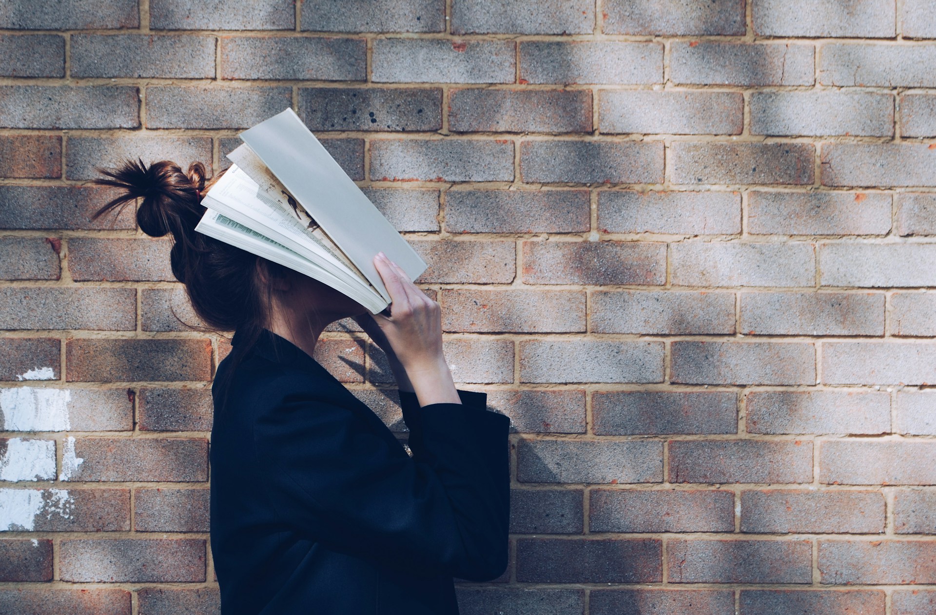 A person holds a big book over their face.