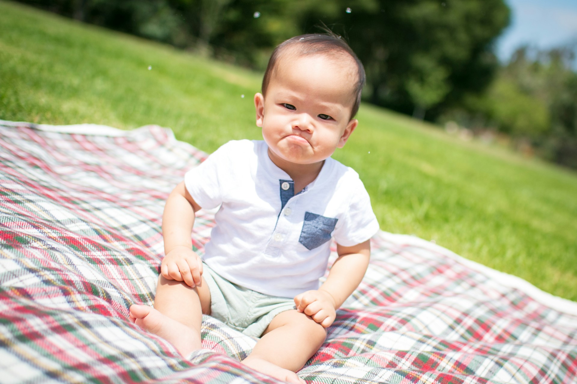 A baby on a plaid picnic blanket frowns dramatically.