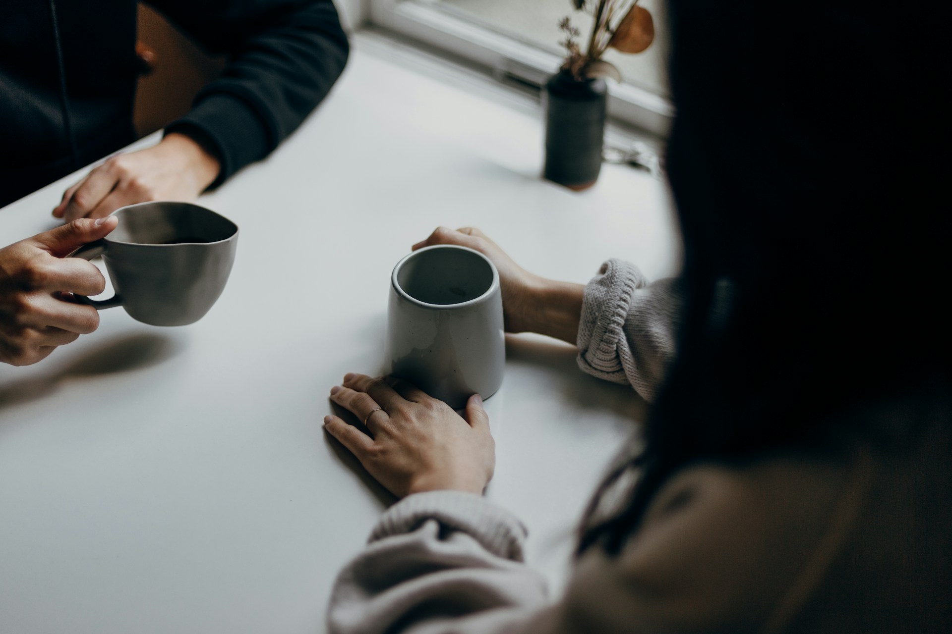 Two sets of hands hold coffee cups at a cafe table.