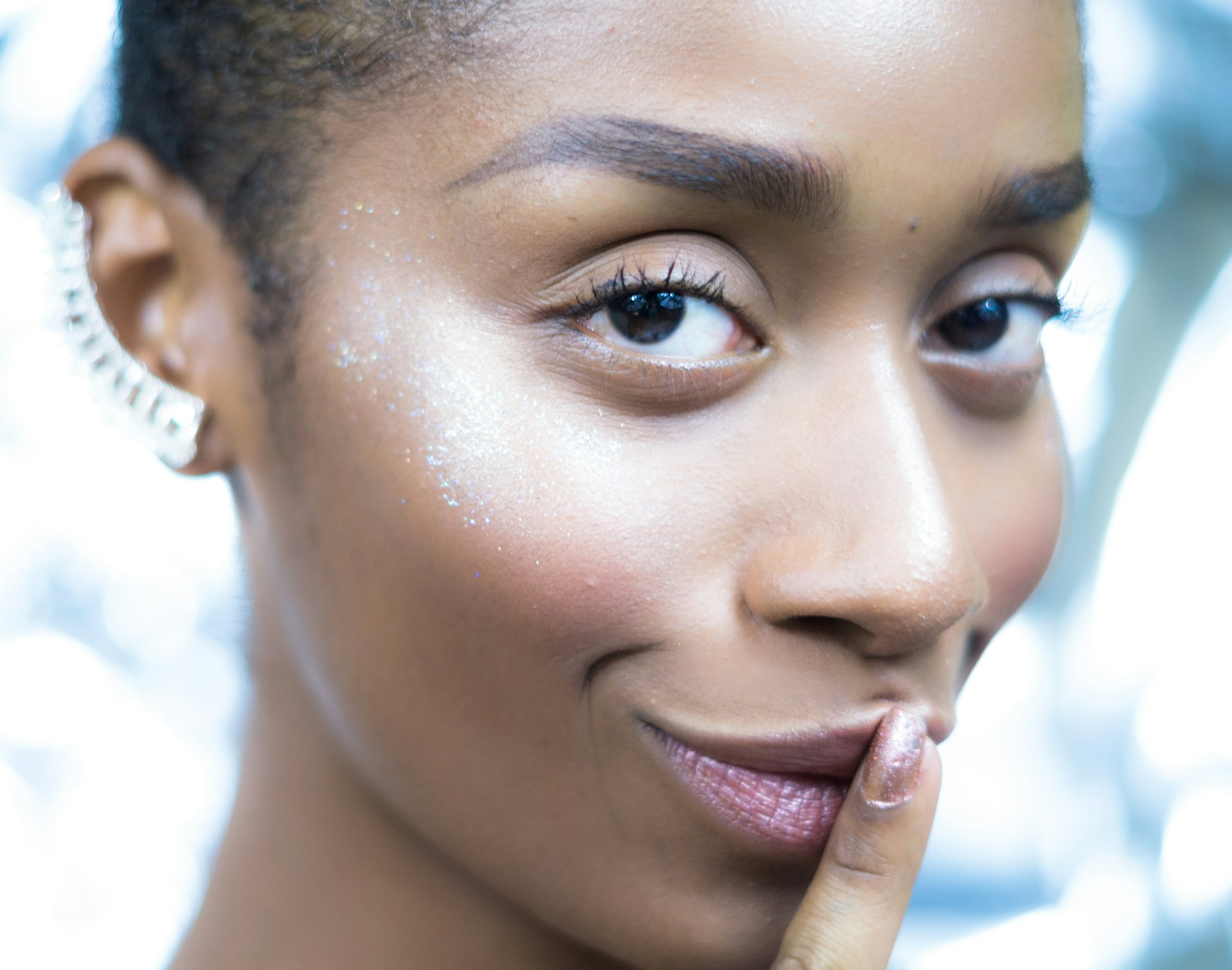 A person smiles and holds a finger to their lips, indicating a secret.