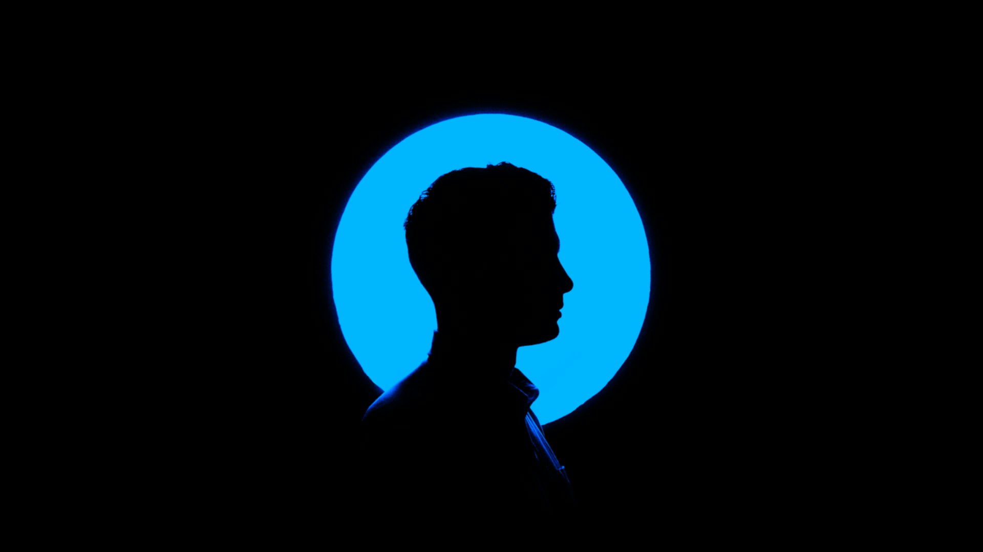 Silhouette of a person's head in profile against a circle of blue light.