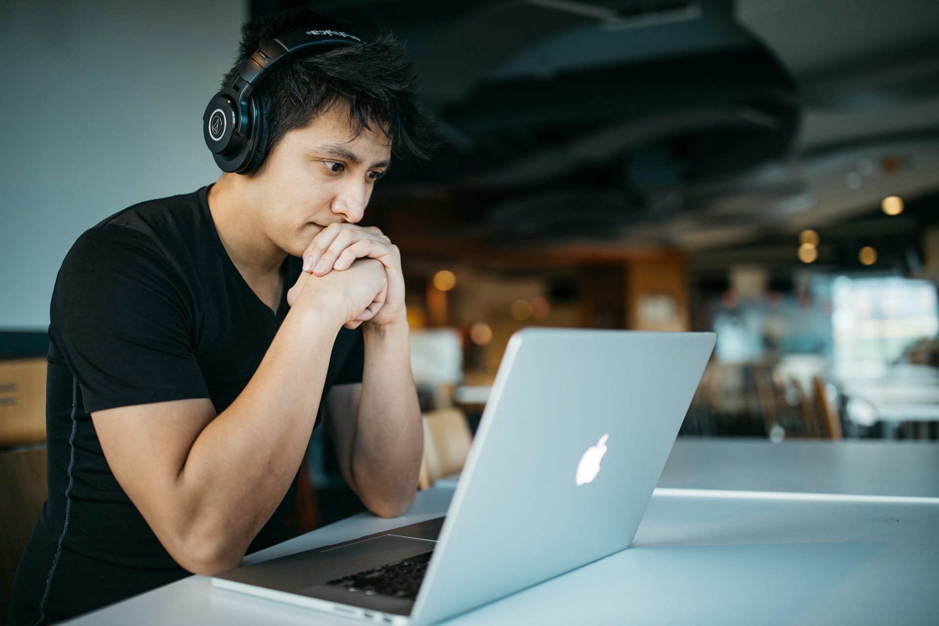 A person wearing headphones stares at a laptop screen, thinking.