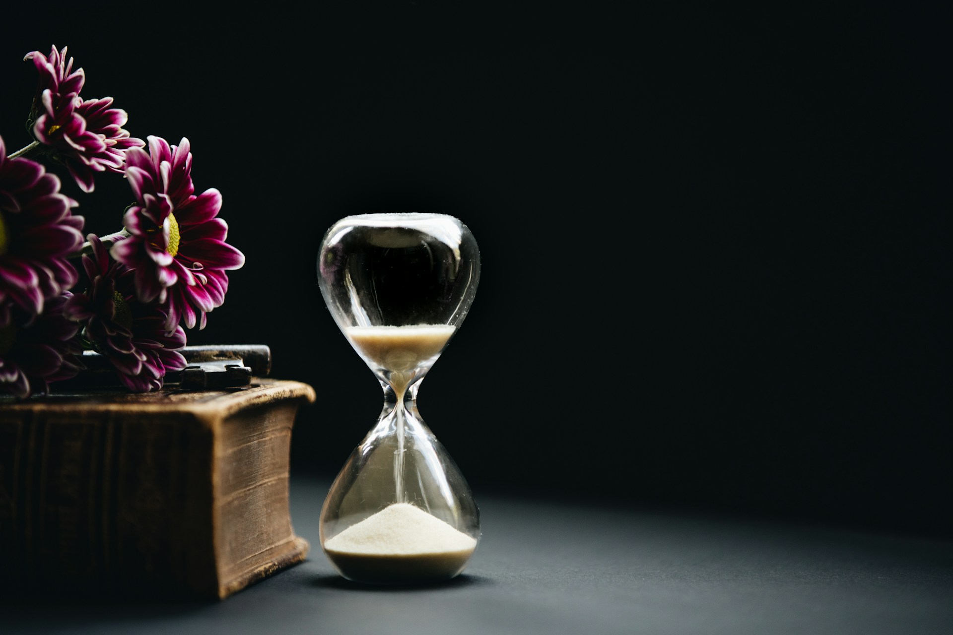 An hourglass stands beside a large book with flowers on it.